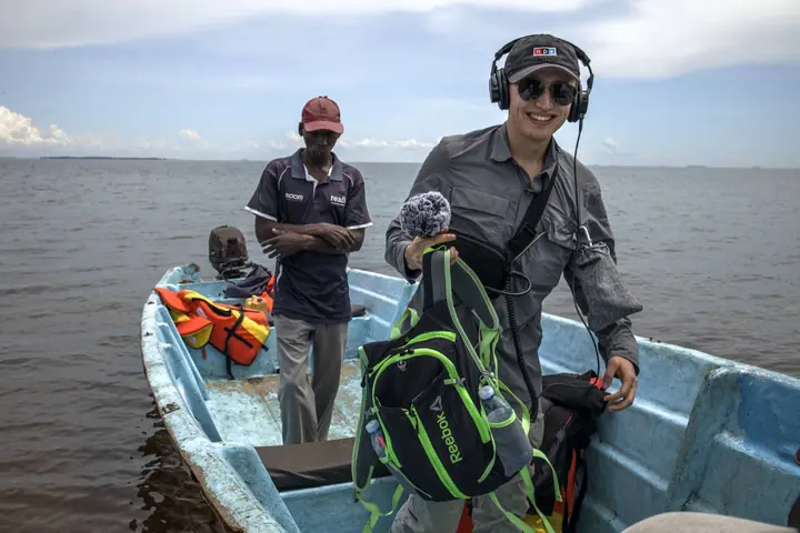 Michal Ruprecht holding a microphone and wearing headphones on a boat on Lake Victoria in Uganda